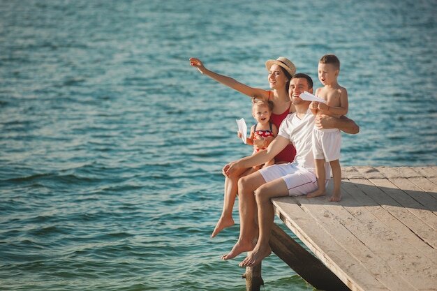 Фото Счастливая веселая семья на пирсе у воды с удовольствием. очаровательные дети играют со своими родителями