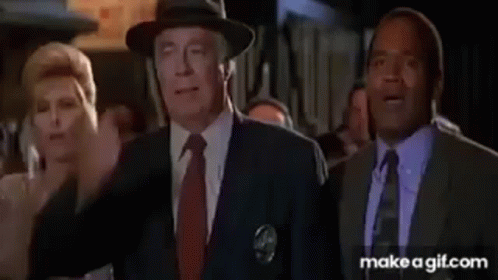 a man in a suit and tie is covering his face with his hand while standing in front of a crowd of people .